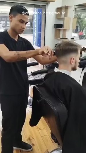Barbeiro em pé finalizando o corte de um cliente no salão