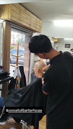 Barbeiro trabalhando junto à vitrine, com a rua ao fundo