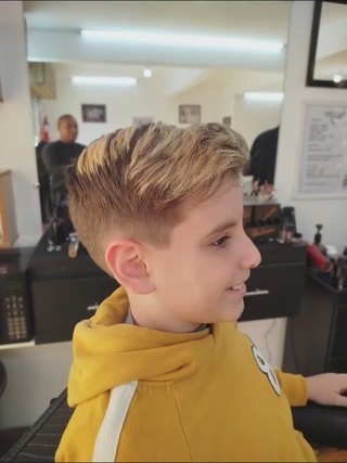 Menino de moletom amarelo sentado na cadeira, cabelo recém-cortado