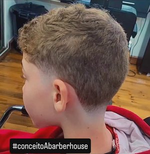 Menino loiro de perfil na cadeira da barbearia