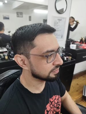 Cliente de óculos na cadeira depois do corte e da barba