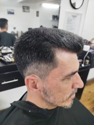 Cliente de perfil na cadeira, laterais baixas e barba aparada