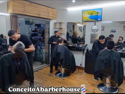 Salão cheio, três barbeiros atendendo ao mesmo tempo, piso de madeira e espelhos