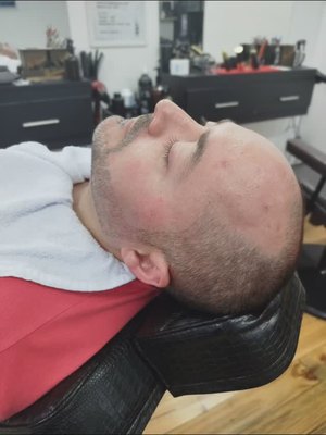 Cliente reclinado na cadeira com toalha branca no pescoço durante a barba